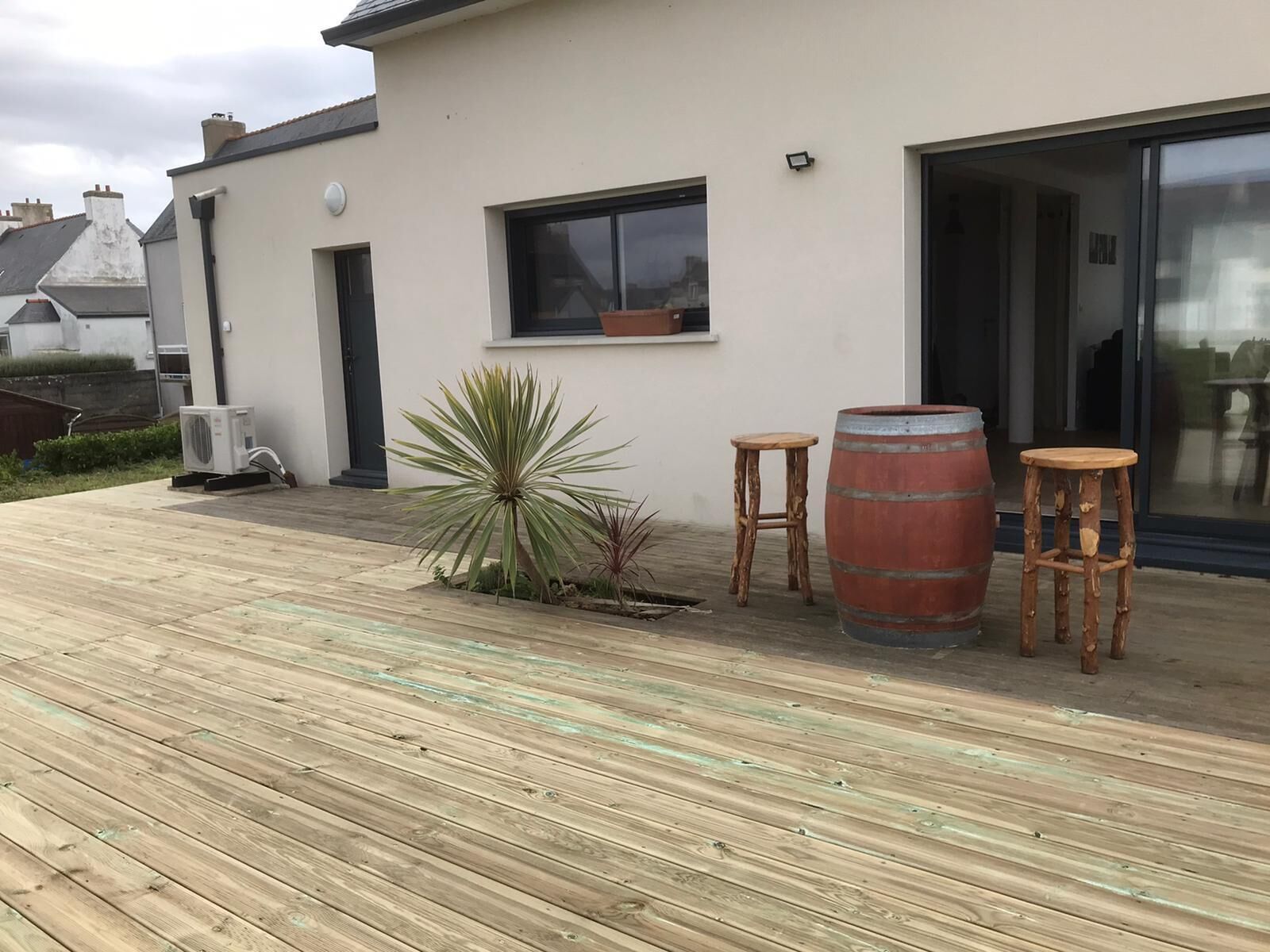 A wooden deck with a potted plant, two stools, and a barrel.
