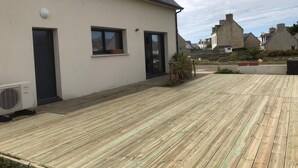 Ein modernes Haus mit einer Holzterrasse, einer schwarzen Tür und einem Fenster.