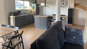 Eine moderne Küche mit einer zentralen Kochinsel, einem Essbereich mit einer Couch und einer Treppe.