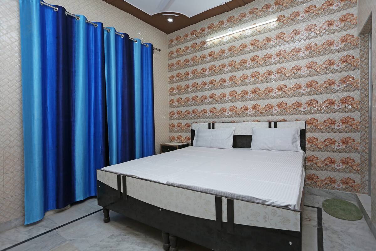 Een slaapkamer met een bed, gordijnen, een nachtkastje en een bloemen behang.