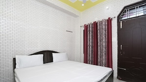 A bedroom with a bed, white brick walls, a dark wooden door, and a red patterned curtain.