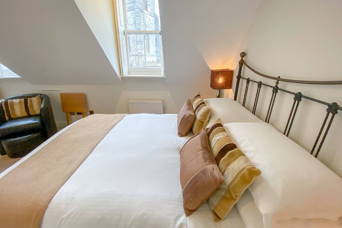 A bedroom with a bed, a chair, a lamp, and a window.