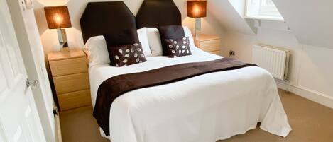 A bedroom with a bed, two bedside tables, a nightstand, a radiator, and a window.