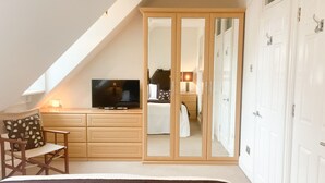 Ein Schlafzimmer mit Fernseher, Bett, Sessel, Kleiderschrank und Spiegel.