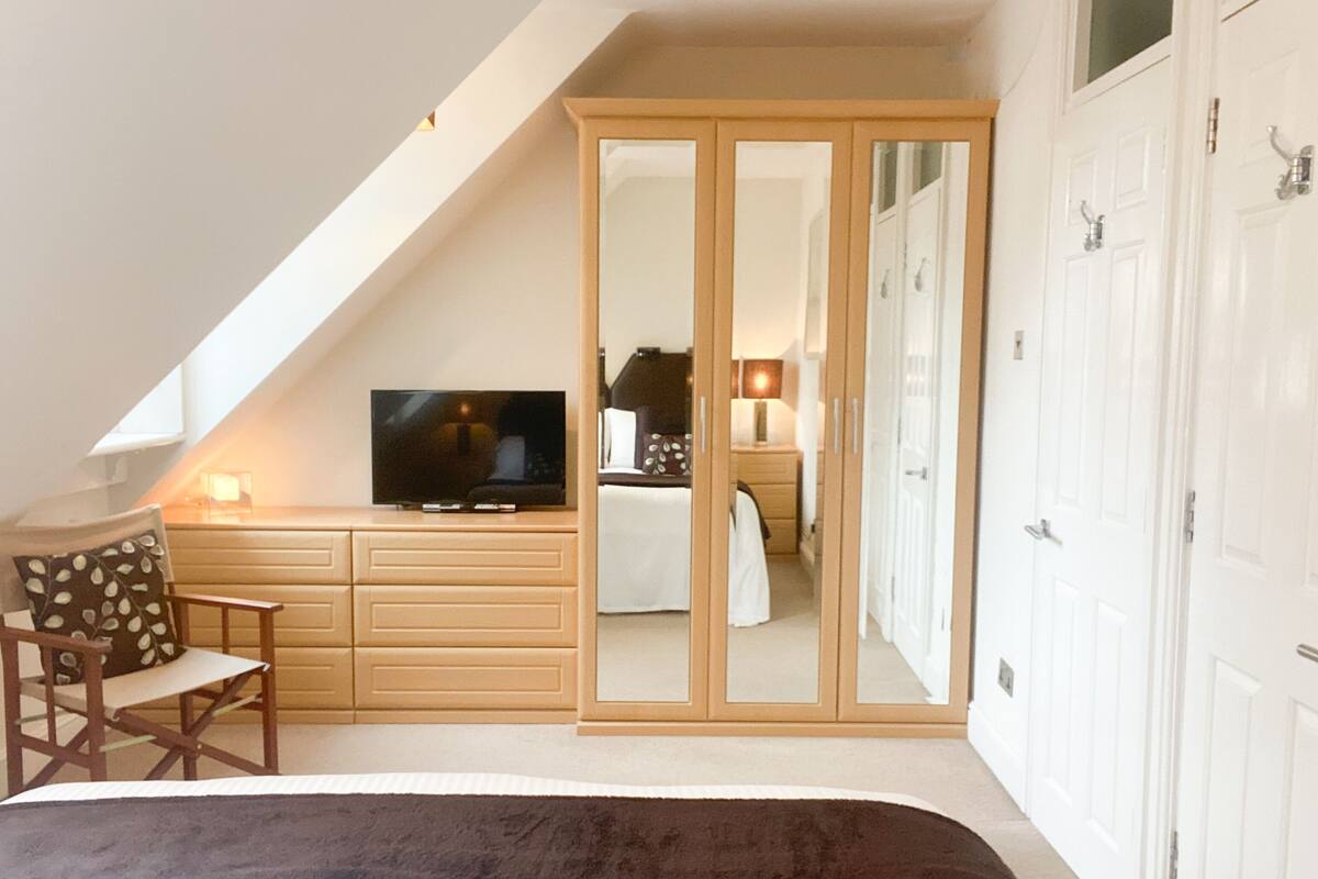 A bedroom with a TV, a bed, a chair, a wardrobe, and a mirror.