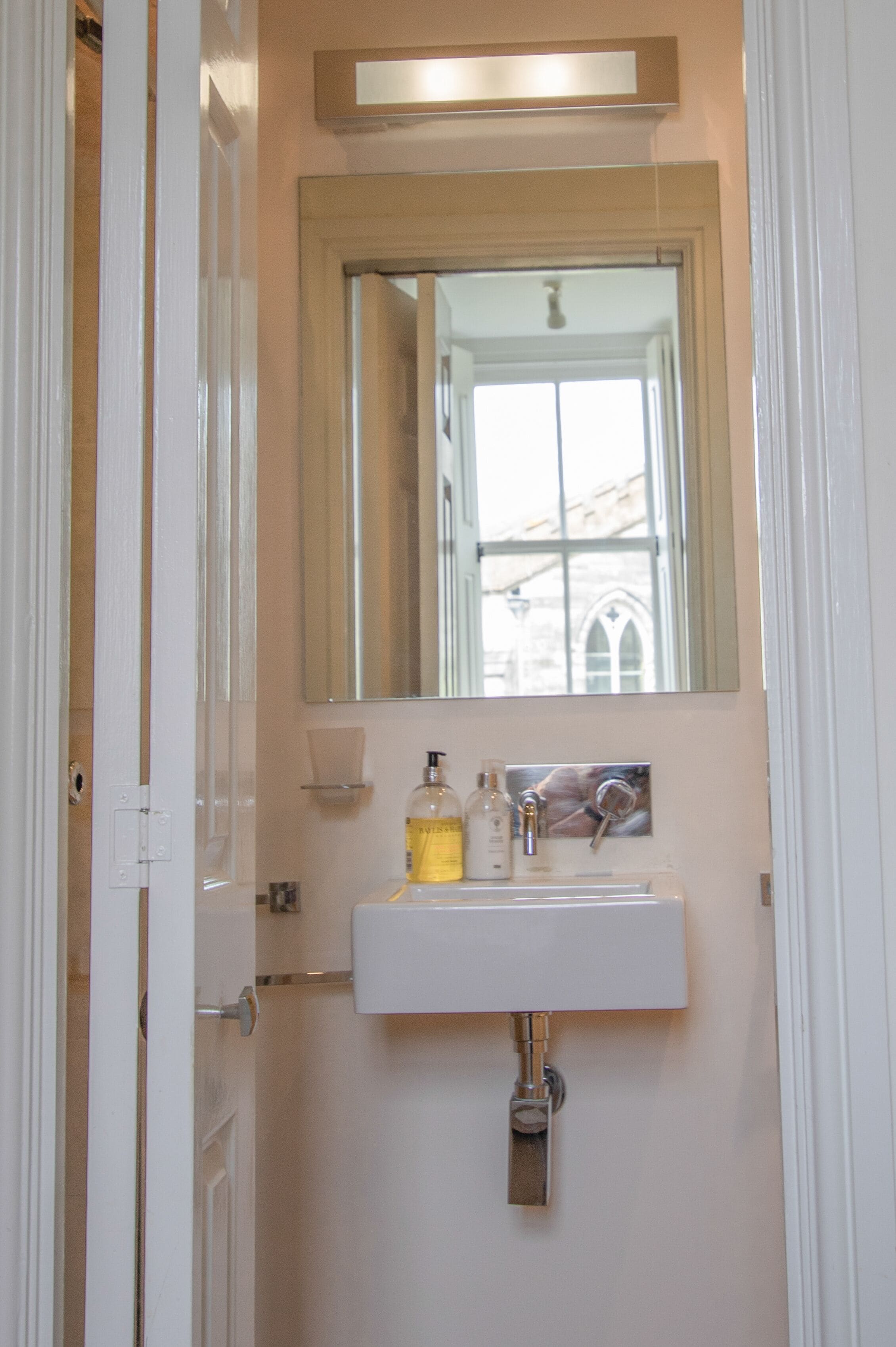 A bathroom with a white sink, a mirror above it, and a window with a view of buildings.