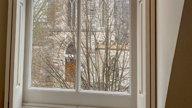 Ein Fenster mit Blick auf einen Steinturm mit rundbogigen Fenstern und einer Uhr.
