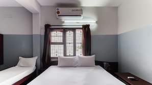 Una camera d'albergo con due letti singoli, un'ampia finestra con tende, un condizionatore d'aria e un comodino con un telecomando.