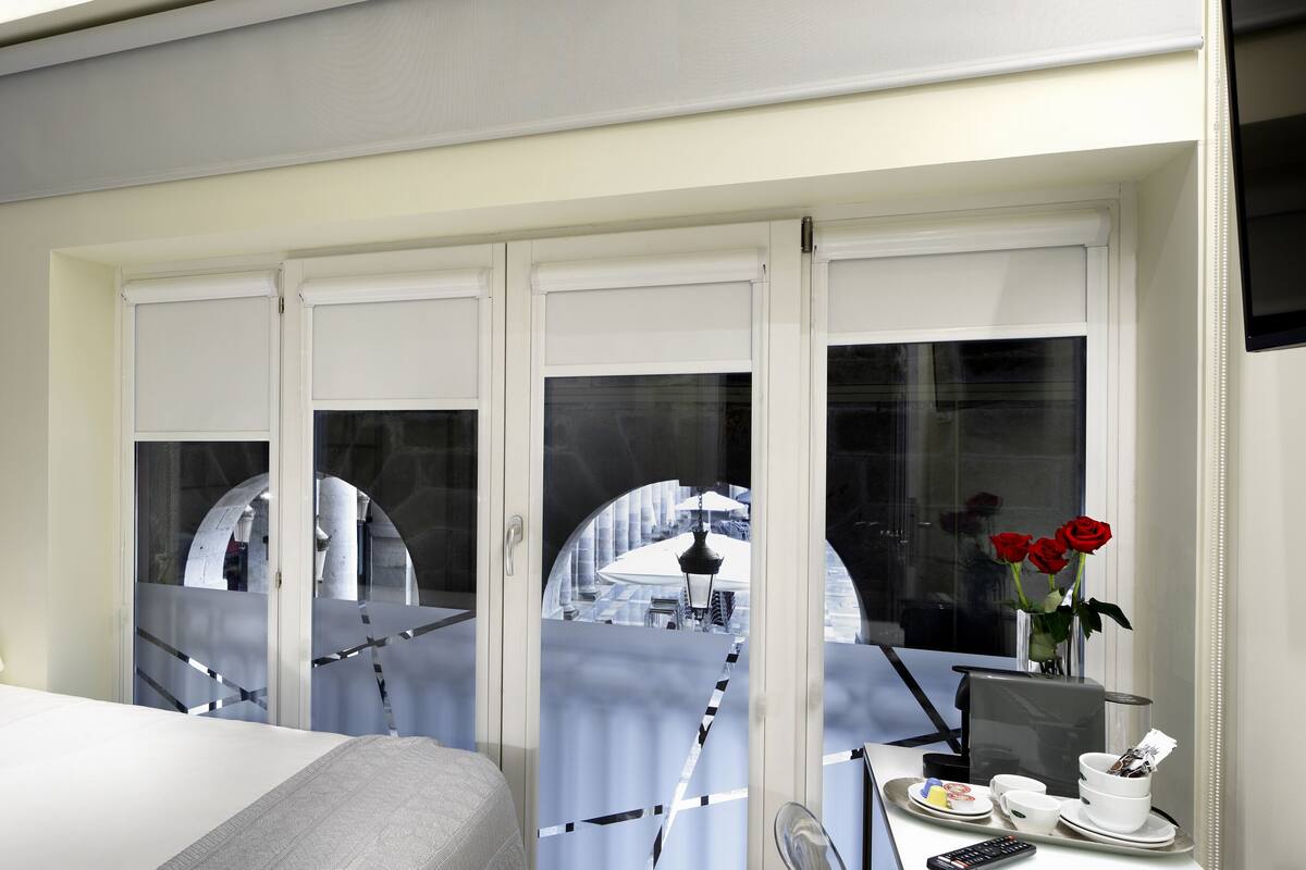 A modern hotel room with a bed, a desk with a computer, and a view of the outside.