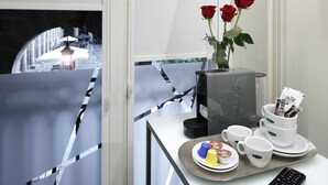 A hotel room with a dining area featuring a table with a tray of food, a coffee maker, and a vase with red roses. - Pensión Plaza Nueva (Bilbao)