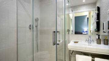 Un bagno moderno con doccia vetrata, un lavandino bianco con rubinetto dorato e uno specchio grande sopra il lavandino.