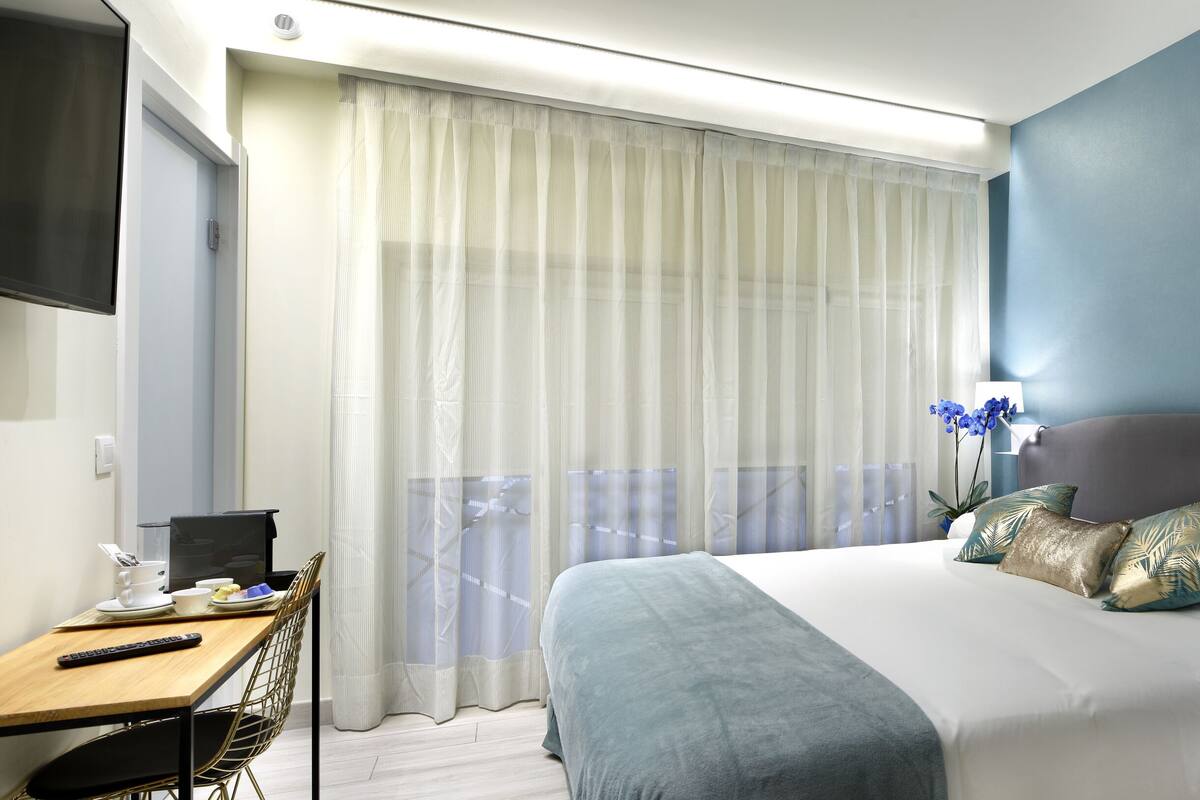 A hotel room with a bed, a desk, a chair, a TV, and a window with curtains.