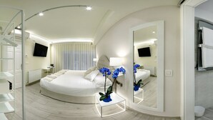 A modern hotel room with a curved bed, a large mirror, a bathroom with a glass shower, and a white color scheme. - Pensión Plaza Nueva (Bilbao)