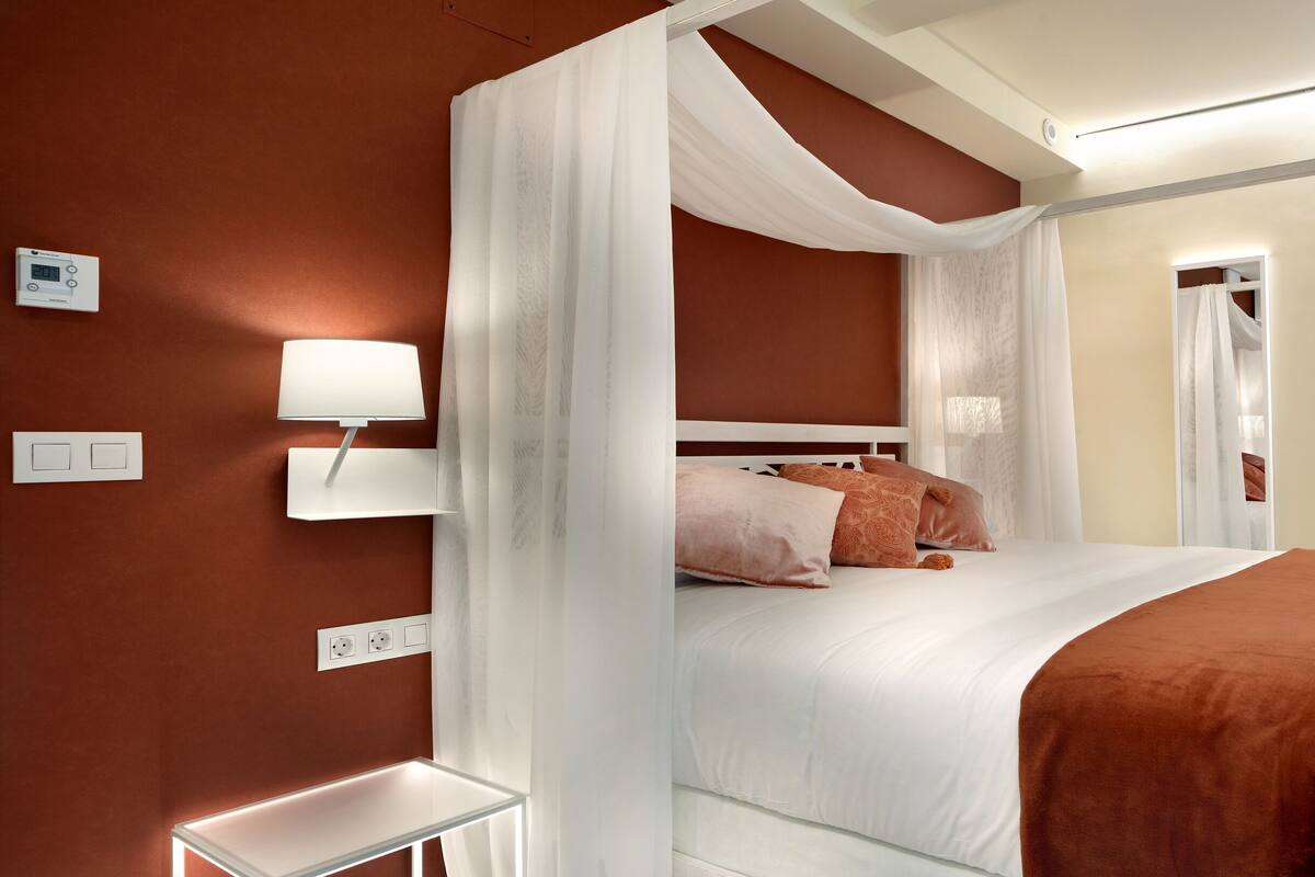 A bedroom with a bed, bedside table, lamp, and a desk with a chair.