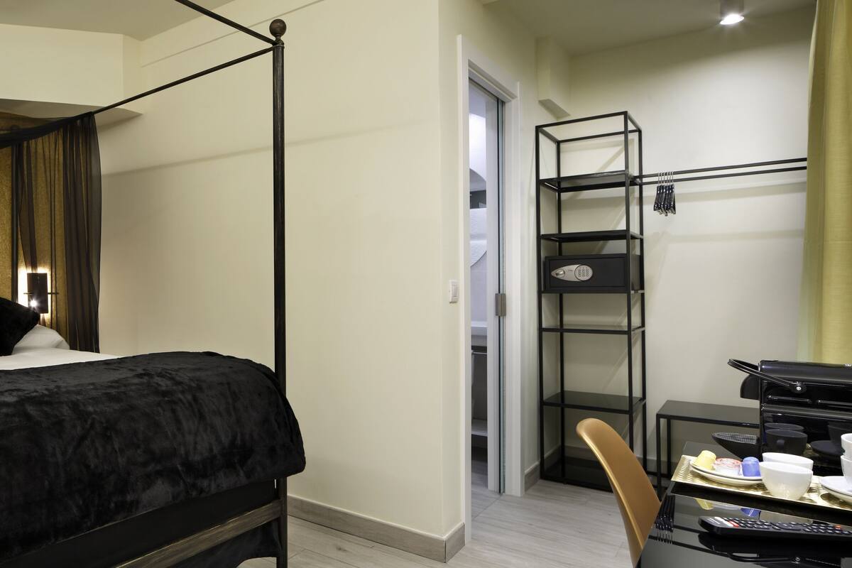 A four-poster bed with a black canopy, a bedside table with a vase of flowers, and a desk with a coffee maker and cups.