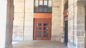 A stone building with a large wooden door, a small balcony, and a tiled floor. - Pensión Plaza Nueva (Bilbao)