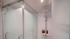 Un baño moderno con cabina de ducha de vidrio, puerta de cristal y repisa con artículos de aseo.
