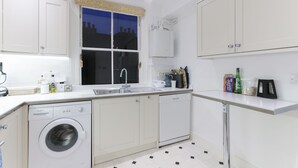 Une cuisine moderne avec des meubles blancs, un lave-linge encastré, un évier et une fenêtre donnant sur des immeubles.