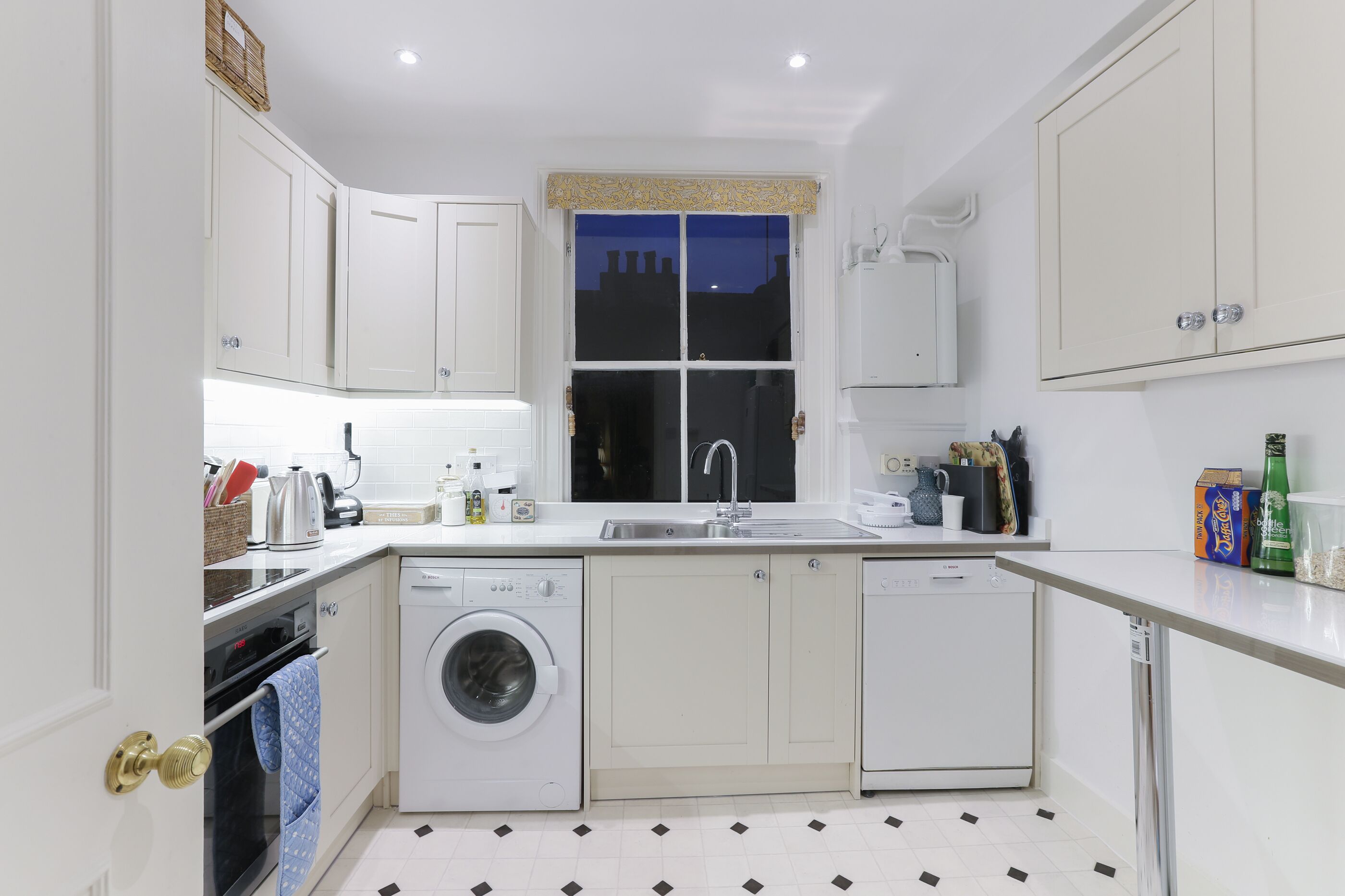A compact kitchen with white cabinetry, a washing machine, a dishwasher, and a window with a view of the night sky.