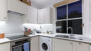 Une cuisine moderne avec des meubles blancs, un lave-linge encastré, un évier en acier inoxydable et une fenêtre donnant sur le paysage urbain.