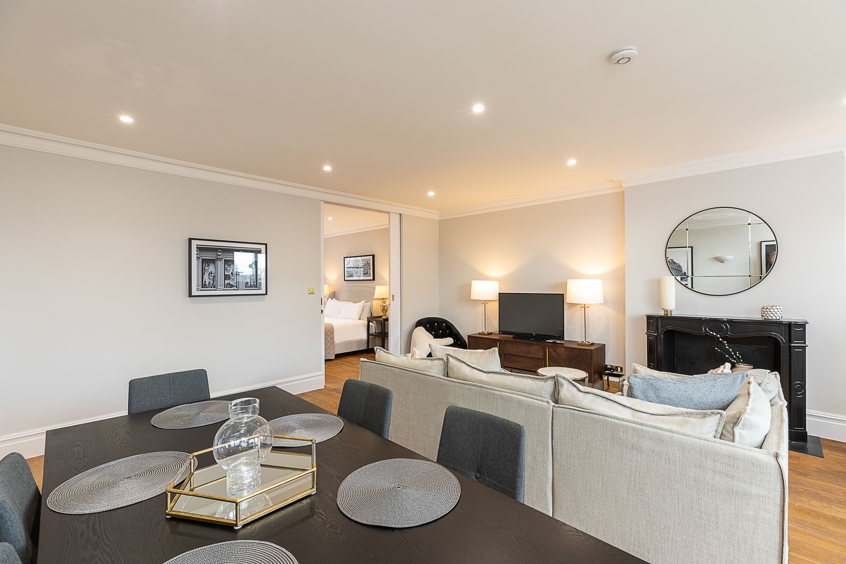 A modern living room with a dark wooden dining table, grey sofas, and a fireplace.