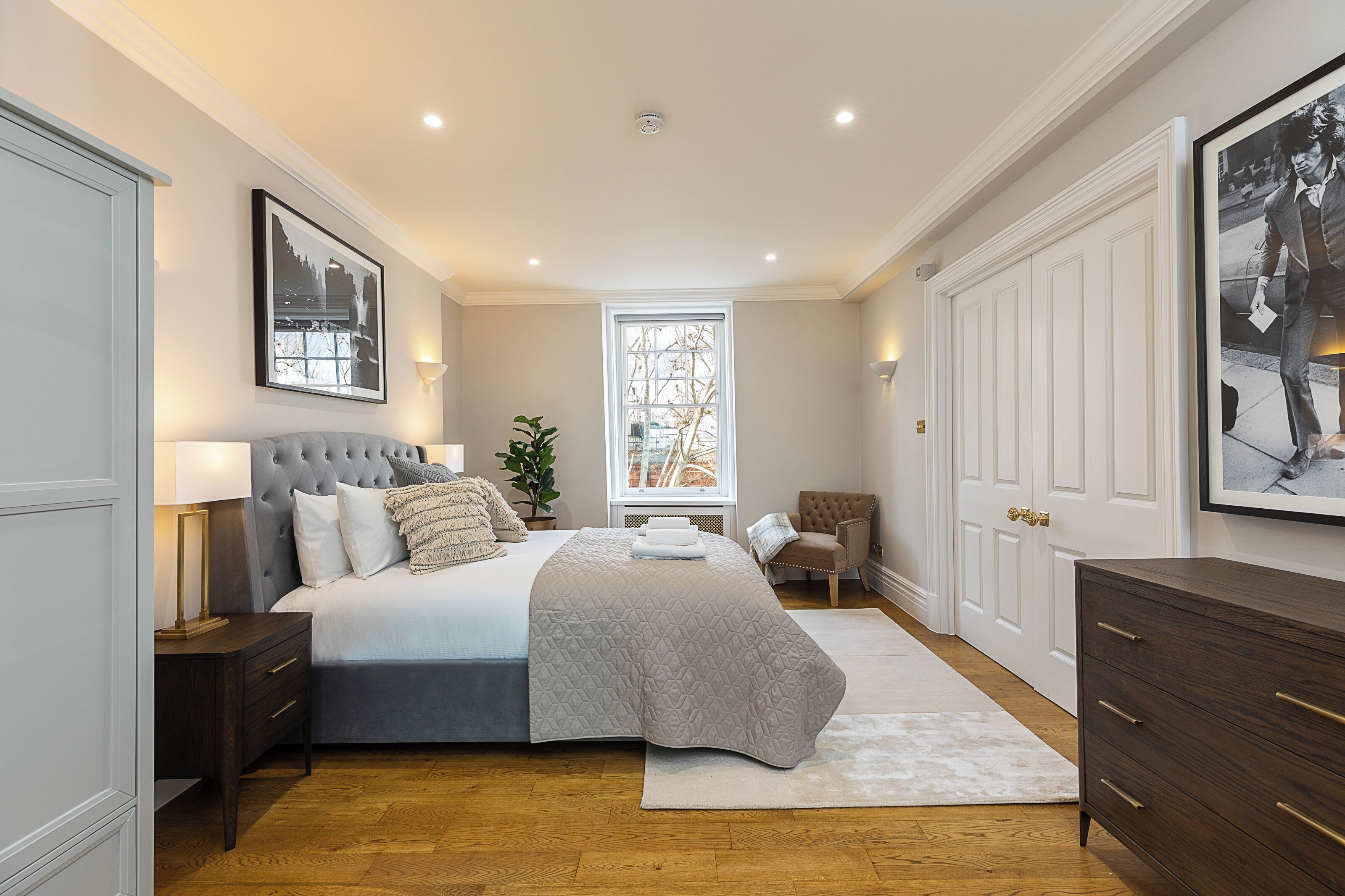 A bedroom with a large bed, a nightstand, a dresser, a window, and a door.