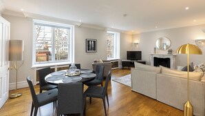 A modern living room with a dining area, large windows, a fireplace, and a television. - JOIVY Astonishing flats near Mayfair & Piccadilly Circus (London)