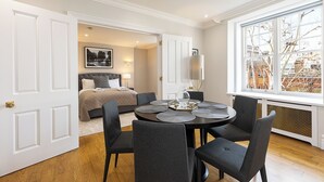 A hotel room with a dining area, a bed, and a large window with a view. - JOIVY Astonishing flats near Mayfair & Piccadilly Circus (London)