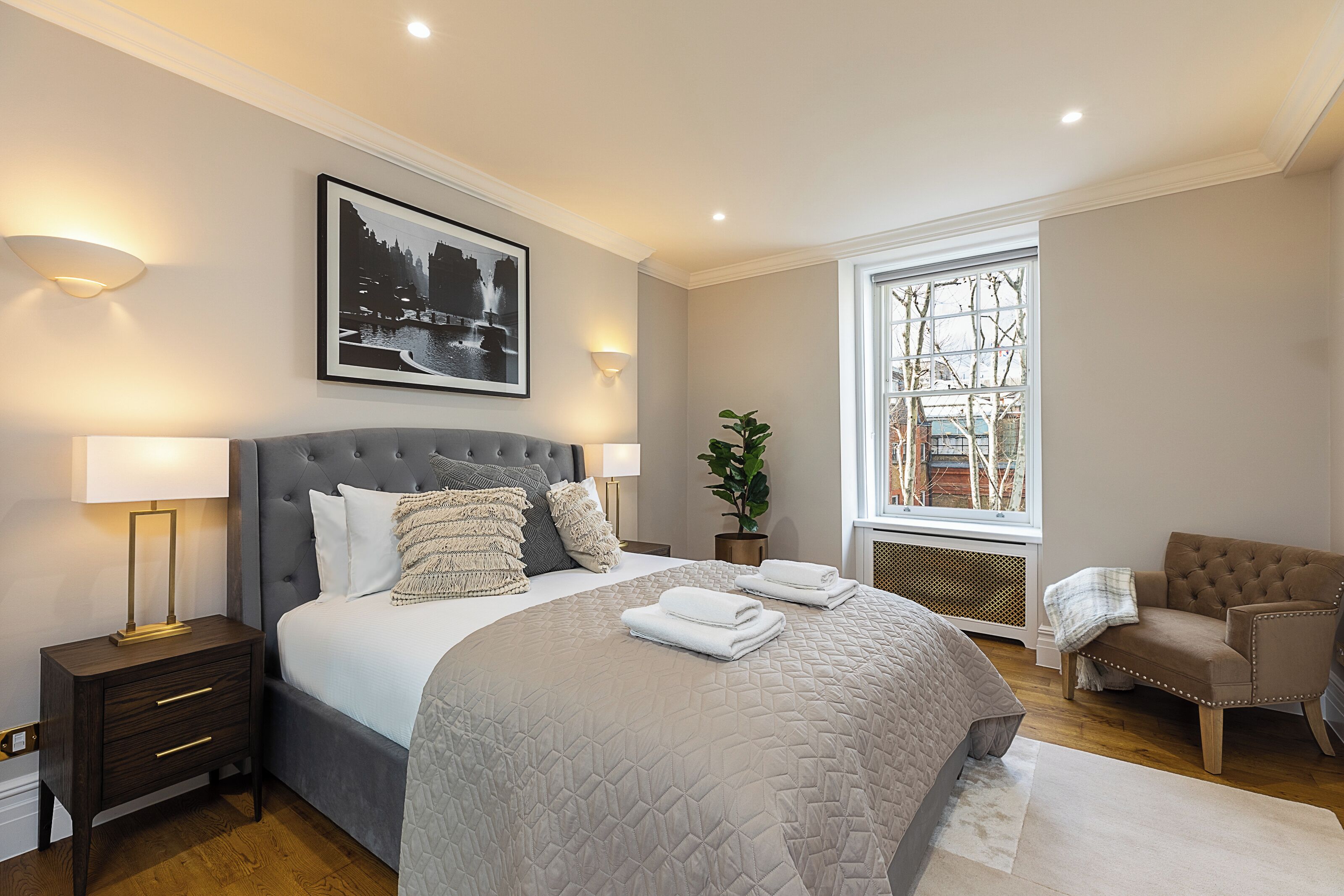 A bedroom with a large bed, bedside lamps, a window with a view, and a chair.