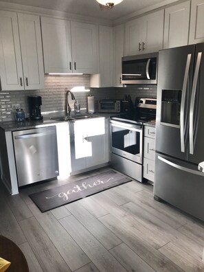 A modern kitchen with white cabinets, stainless steel appliances, a built-in microwave, and a water dispenser.