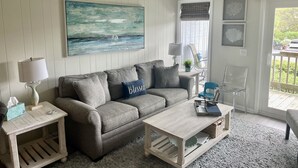 Un salon avec un canapé gris, une table basse, une lampe et un tableau accroché au mur.