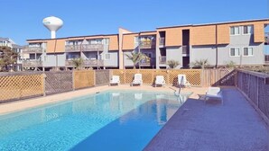 Une piscine avec des chaises longues, un château d’eau et un bâtiment doté de balcons.