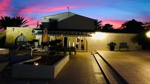 A two-story building with a flat roof and a balcony, surrounded by a stone wall and palm trees. - B&B Casa Pedramala (Benissa)