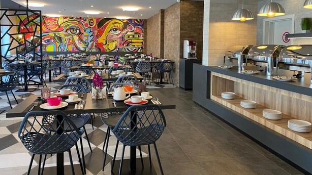 A modern dining area with tables and chairs, a buffet counter, and a colorful mural on the wall. - Metro Hostel (Kyiv)