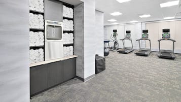 A fitness center with treadmills, a water dispenser, and neatly stacked towels.