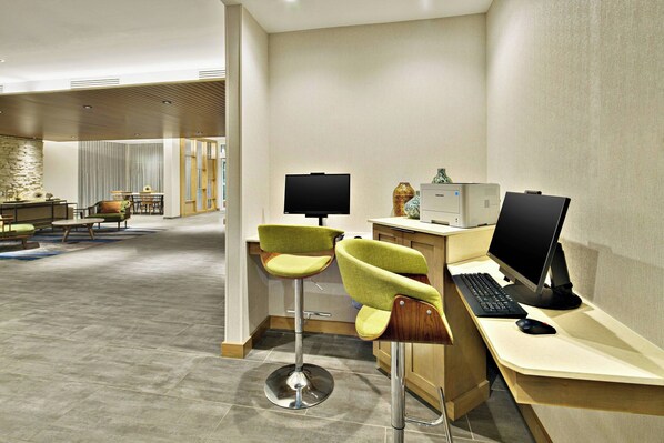 A modern hotel room with a desk, two green chairs, a television, and a computer.