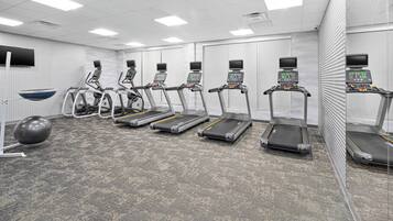 Academia com esteiras, bolas de exercício e um espelho grande.