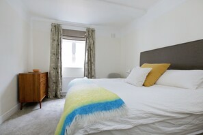 A bedroom with a bed, a wooden dresser, a window with curtains, and a headboard.