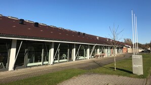 A building with a brown roof, large windows, and a paved walkway. - NIKC Sleepover (Nibe)