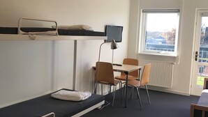 A dormitory room with bunk beds, a desk, chairs, a computer monitor, and a window with a view. - NIKC Sleepover (Nibe)