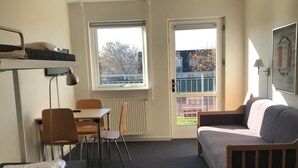 A room with bunk beds, a desk, chairs, a bed, and a window with a view of trees. - NIKC Sleepover (Nibe)