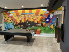 A pool table in a room with a colorful mural depicting Texas State Capital.