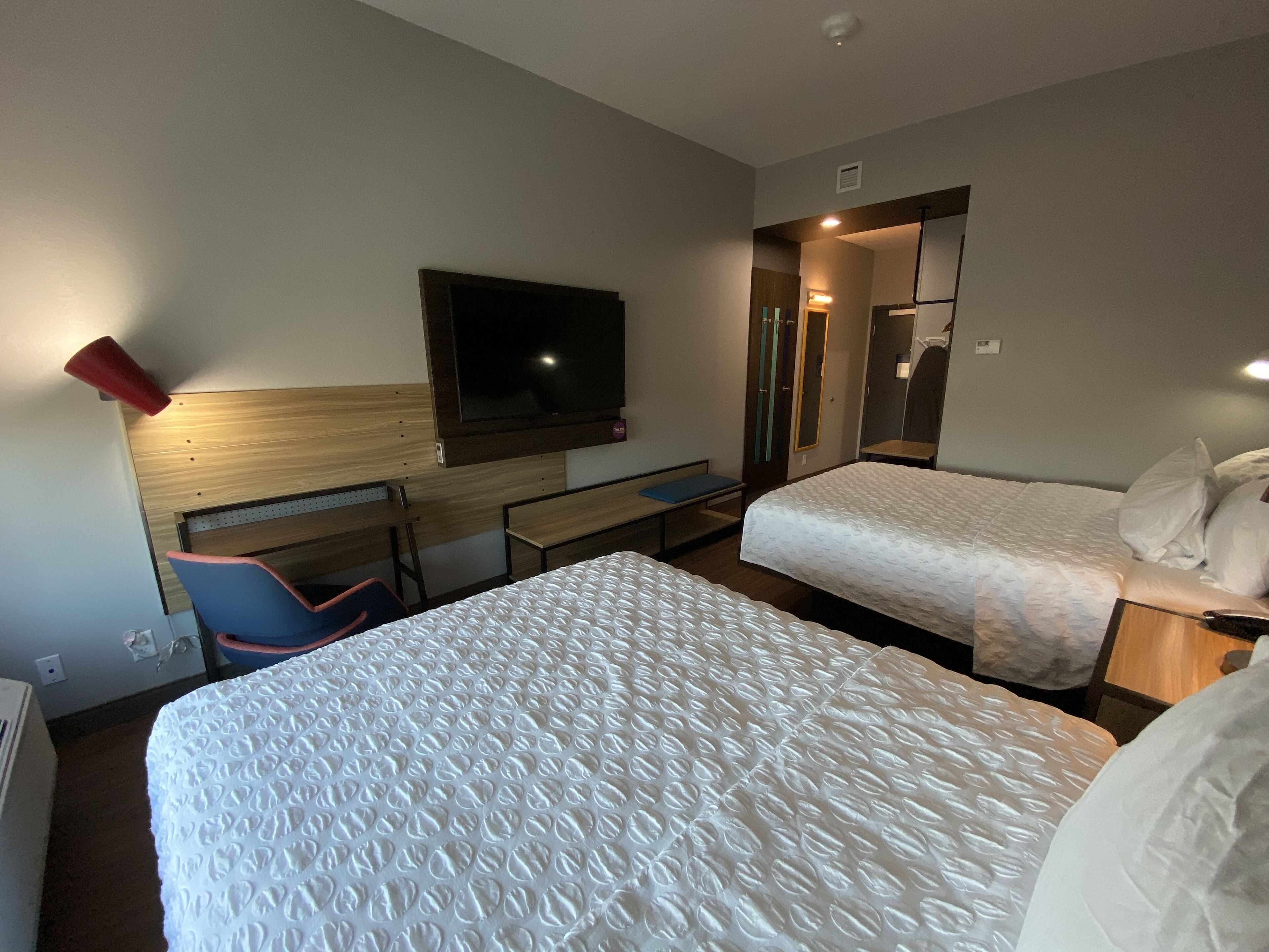 A hotel room with two beds, a desk, a chair, a TV, and a mirror.