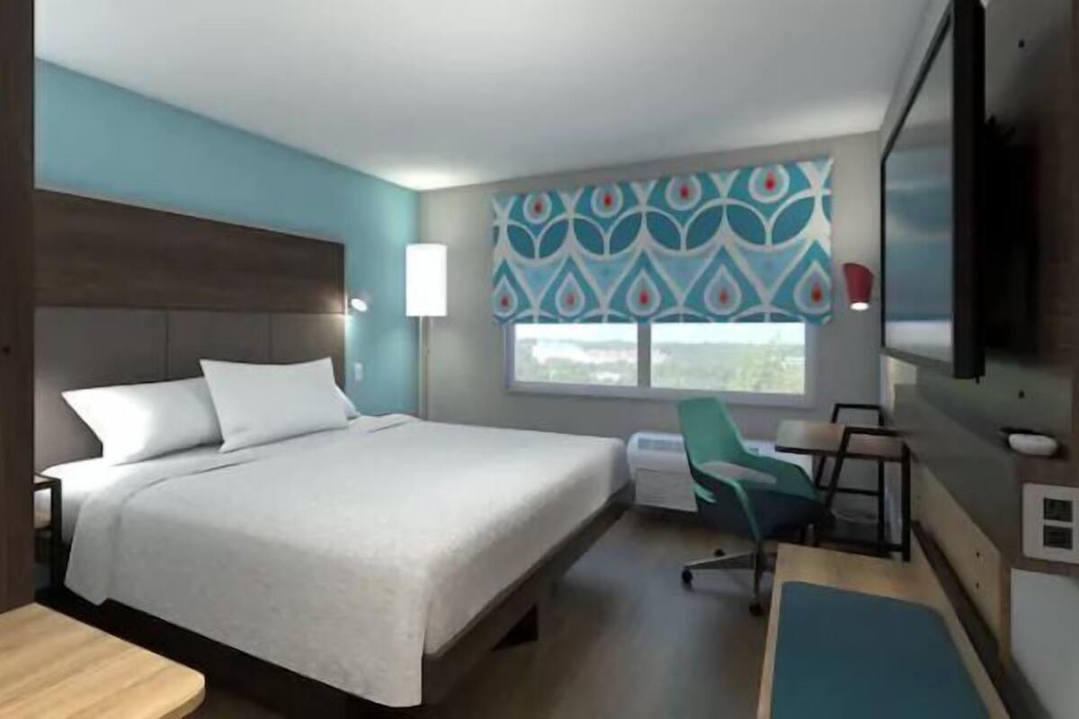 A modern hotel room with a large bed, a desk, a chair, and a TV.