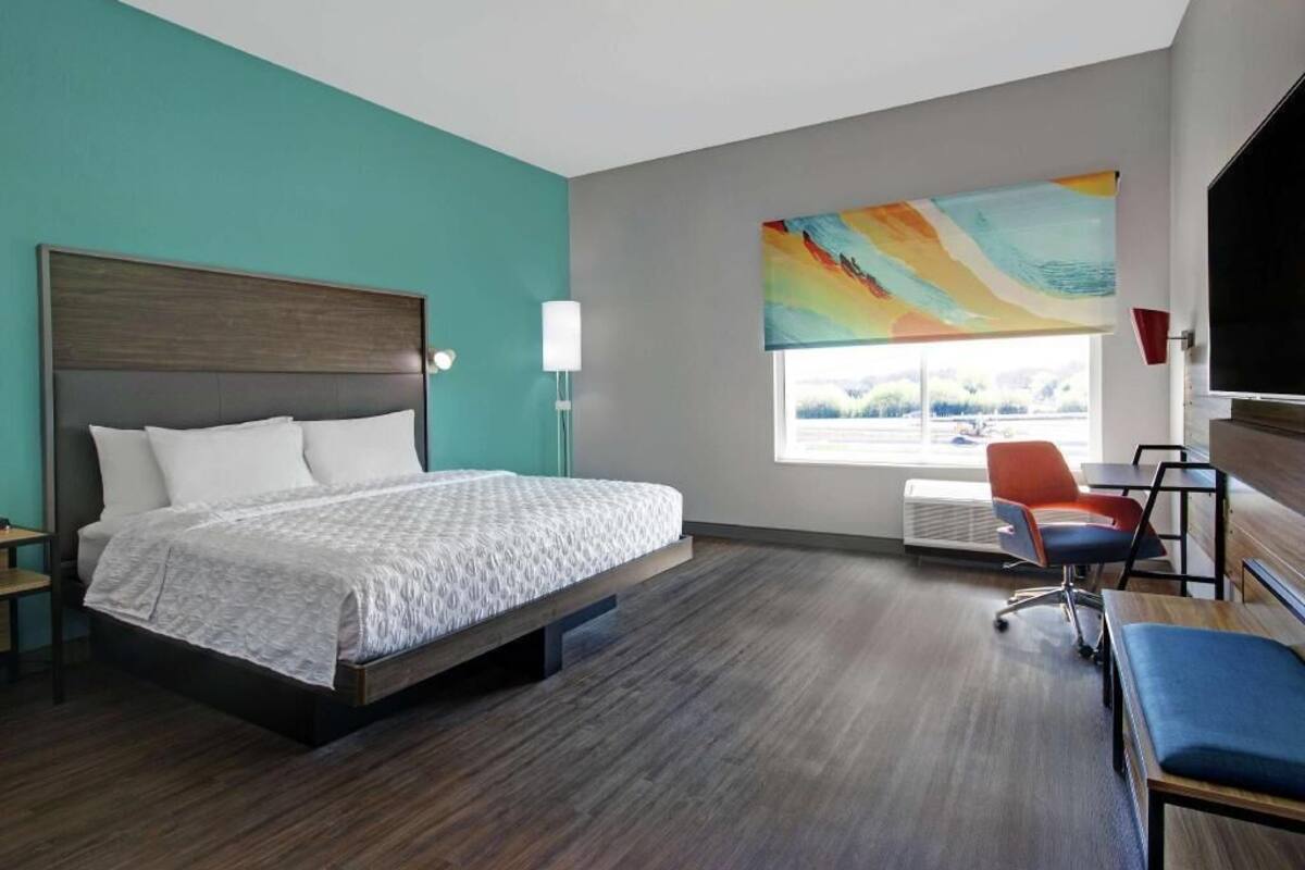 A hotel room with a bed, a desk, a chair, a window with a view, and a painting on the wall.