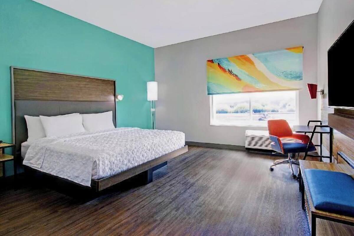 A hotel room with a bed, a desk, a chair, a window, and a painting.
