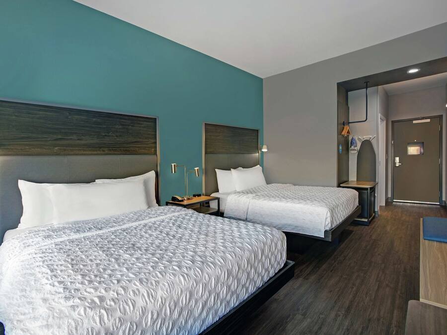 A hotel room with two beds, a desk, and a bathroom visible through an open door.
