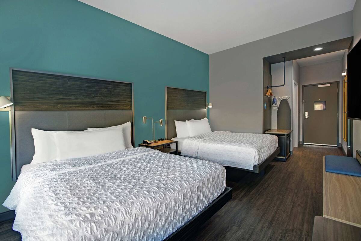 A hotel room with two beds, a desk, a chair, and a door leading to a bathroom.
