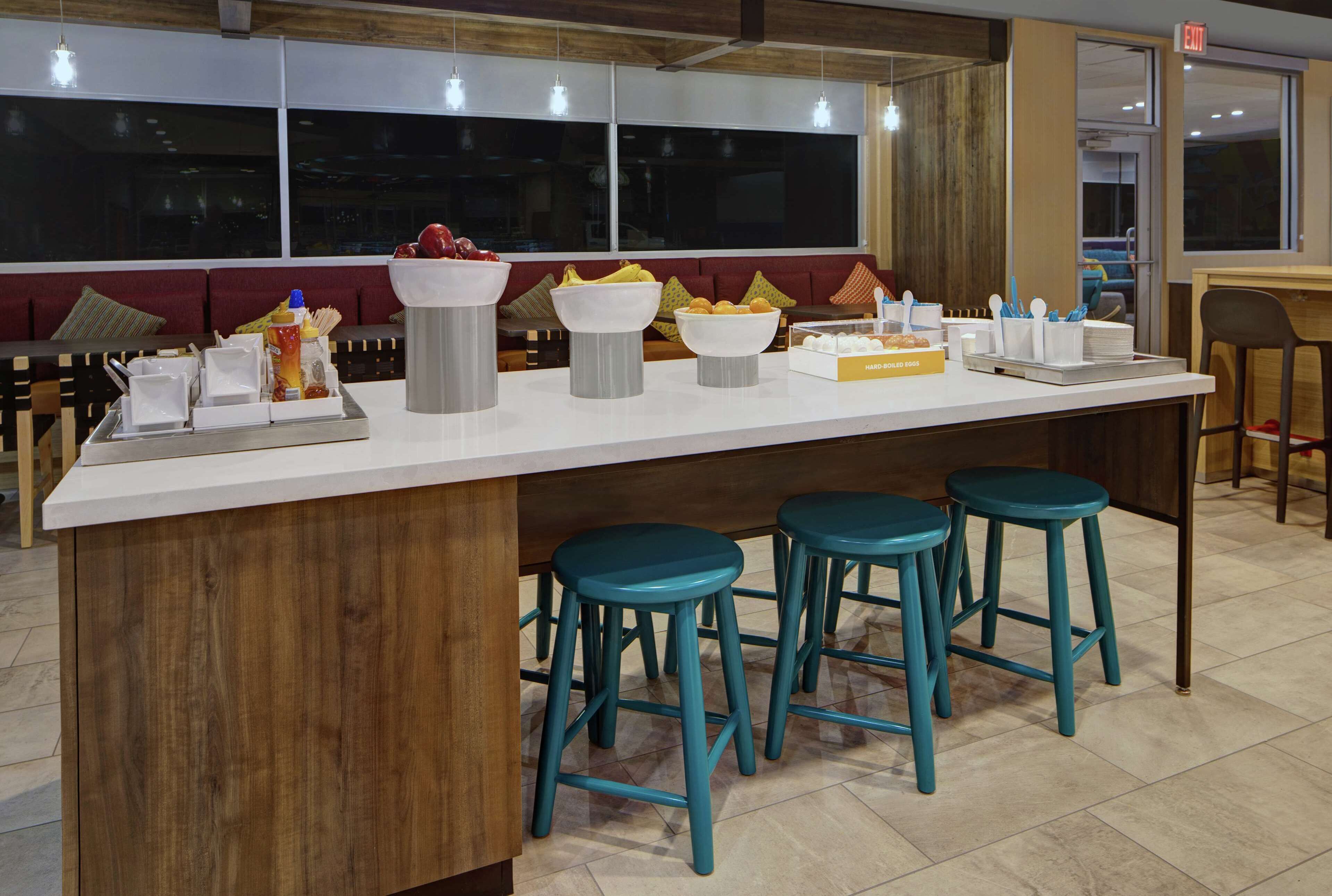 A bar area with stools, a counter with food and drink items, and a seating area with a couch and cushions.