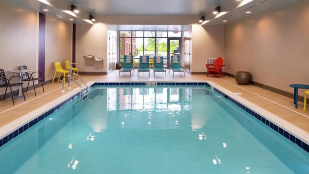 A swimming pool with chairs and tables, a clear view of the outdoors, and a tiled floor.